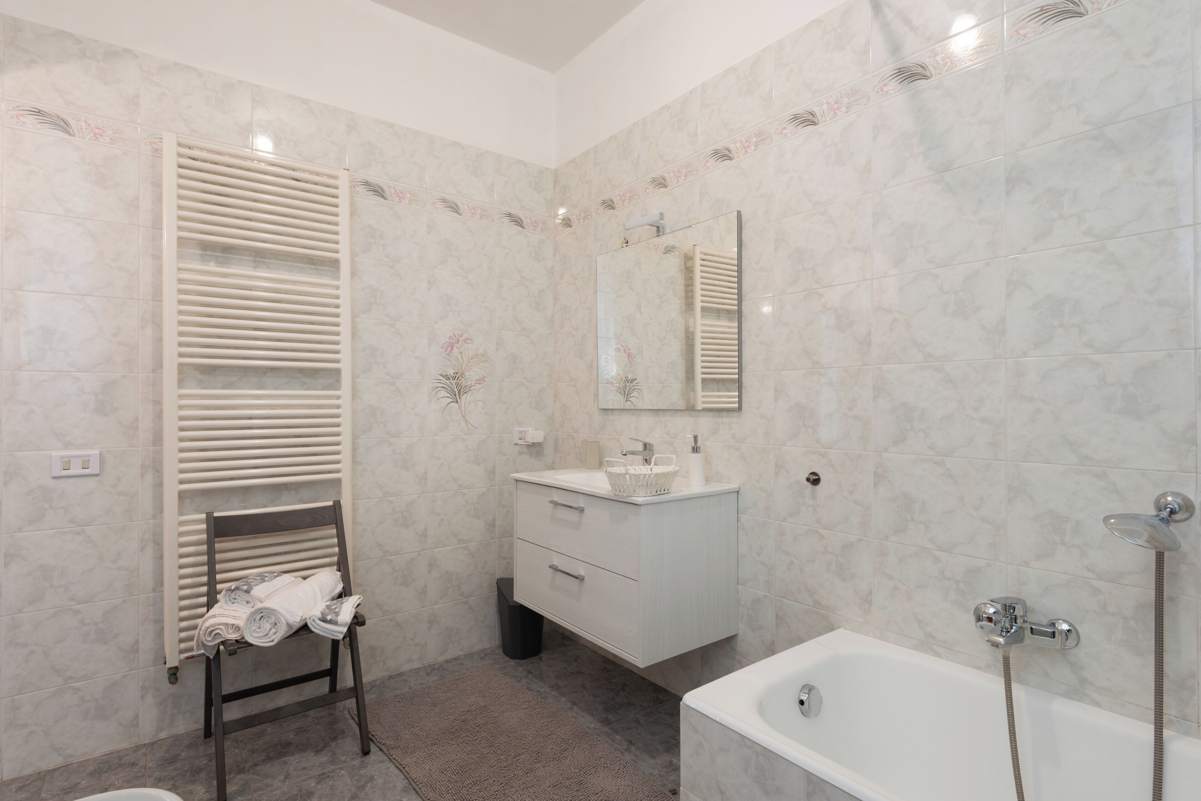 A bathroom with a bathtub, a sink, a mirror, a towel rack, and a radiator.