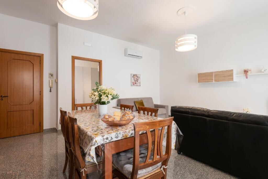 Un comedor con mesa de madera, sillas, un florero y un sofá negro.