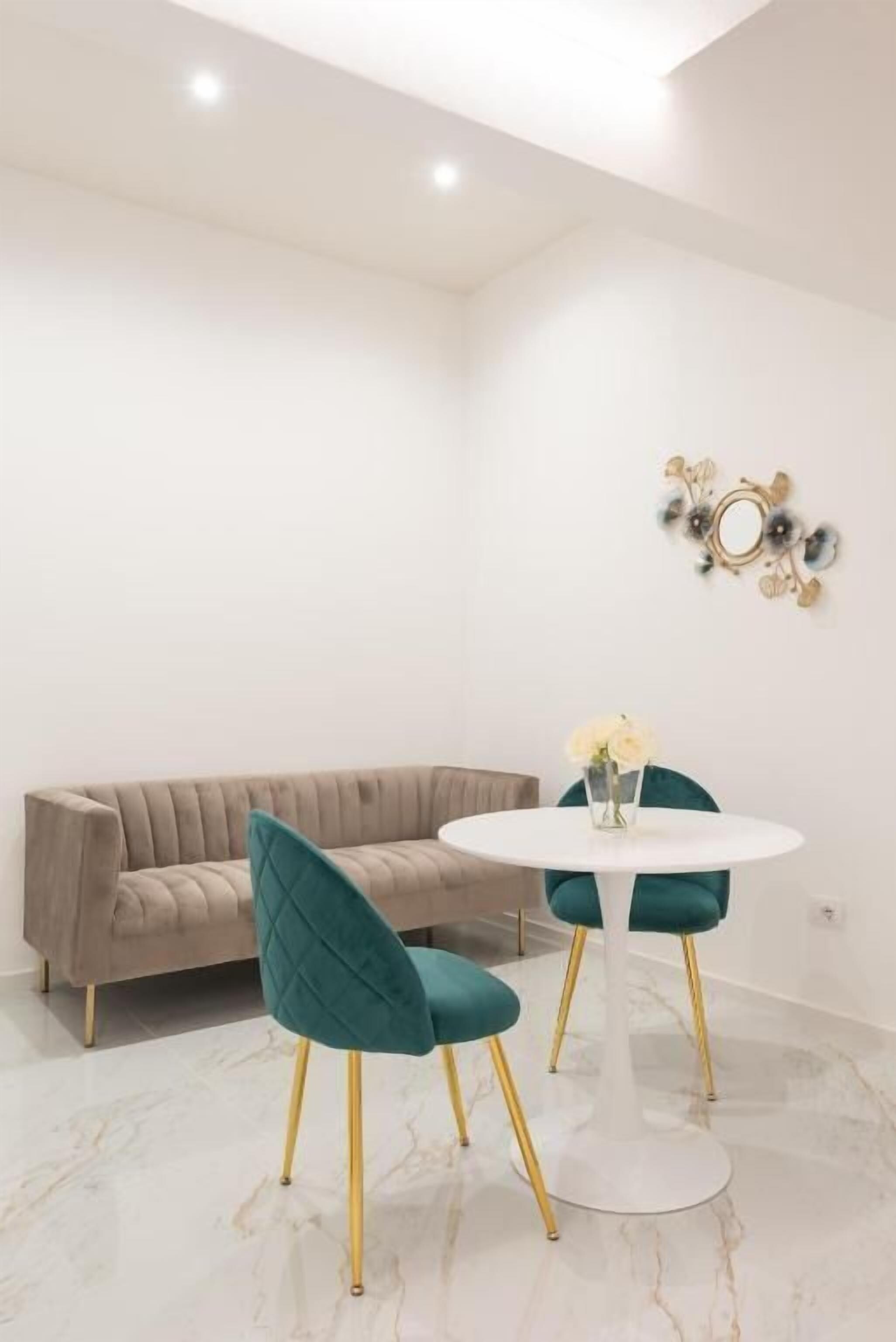 A modern room with a beige sofa, teal chairs, a white round table, and a decorative wall piece.