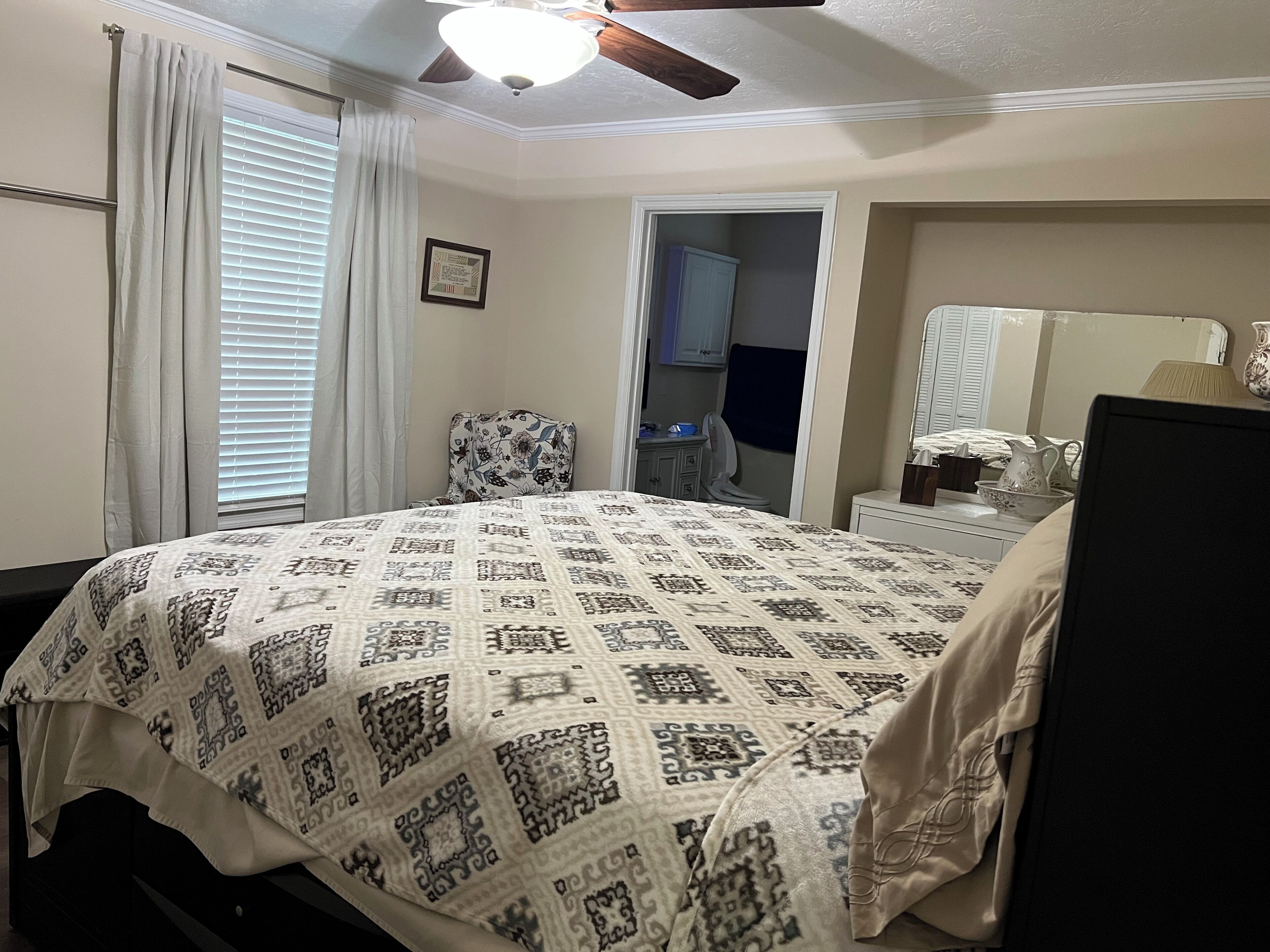 A bedroom with a bed, a chair, a desk, a mirror, and a ceiling fan.