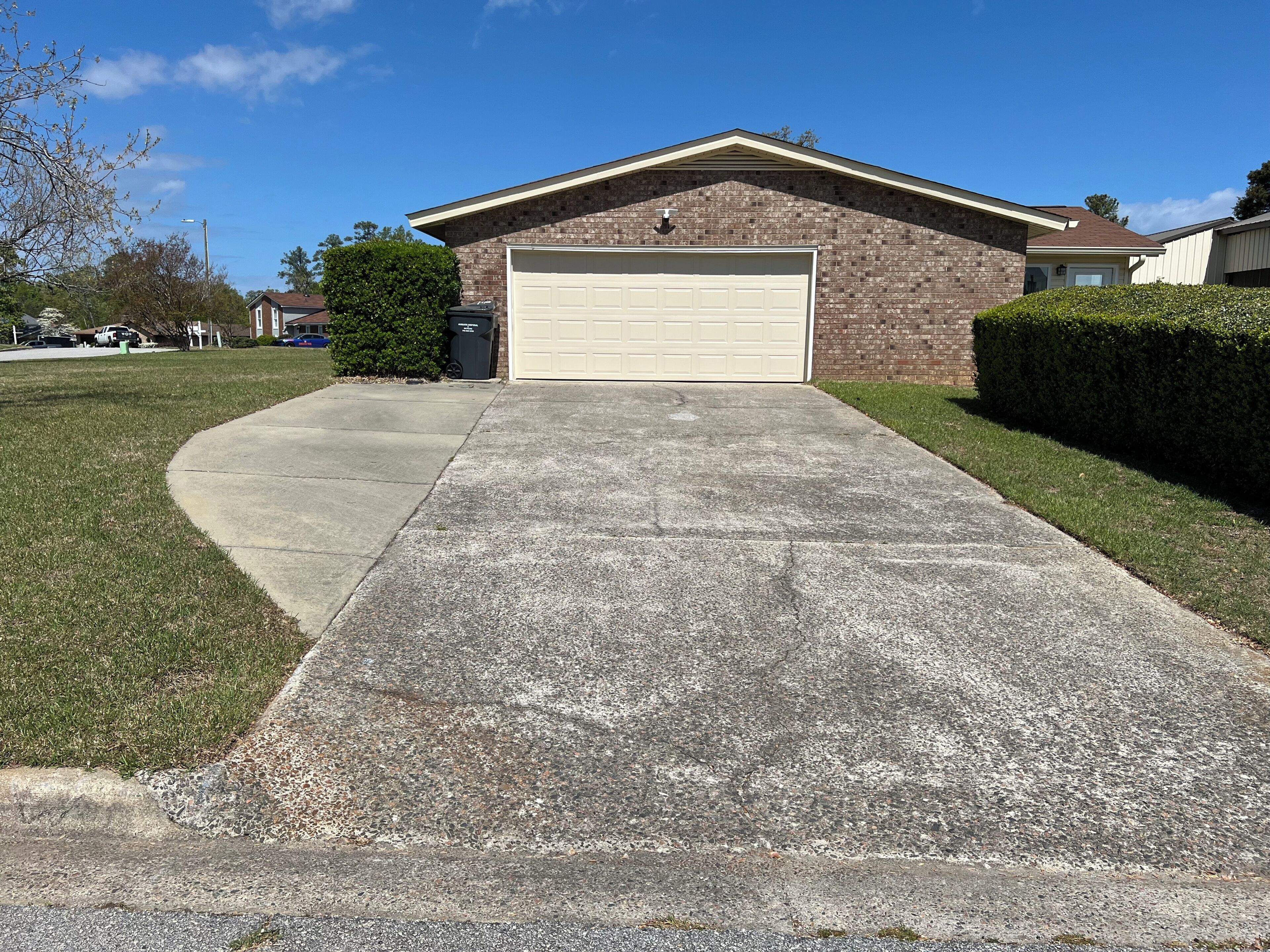 A residential driveway leading to a garage, surrounded by grass and a hedge.