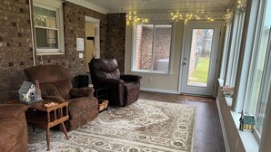 A living room with a brick wall, leather recliners, a patterned rug, and a large window with a view of the outdoors. - Restful ranch, 4.6 miles from The Masters. 3-bedroom house, 2 full baths (Martinez)