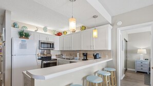 Une cuisine moderne avec des meubles blancs, un îlot central doté de tabourets, un four à micro-ondes et un réfrigérateur.