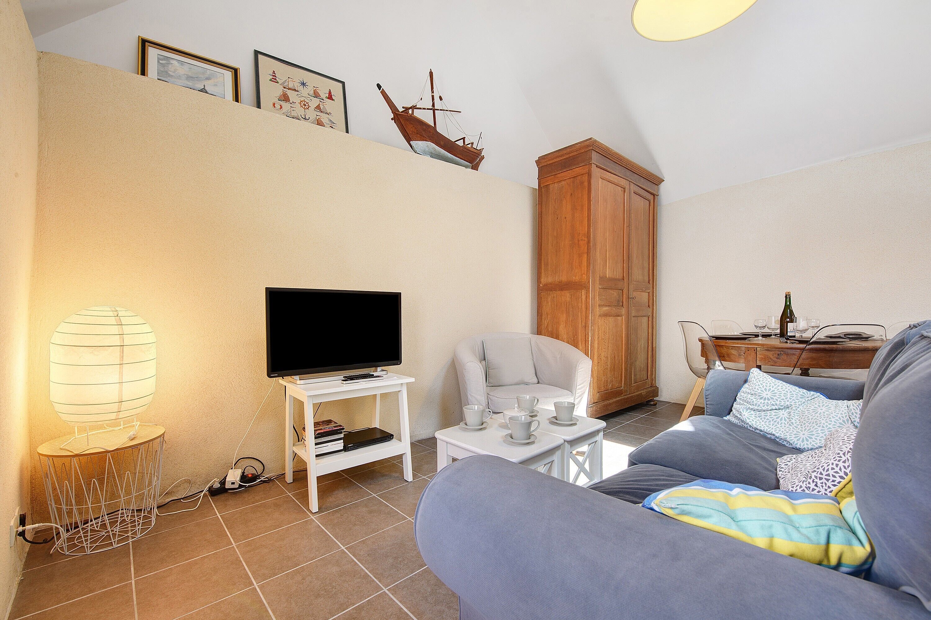 Een woonkamer met een televisie, een bank, een tafel met kopjes, een lamp en een decoratie van een schip aan de muur.