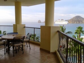 Un balcone con tavolo e sedie, vista sul mare e una nave da crociera in lontananza.