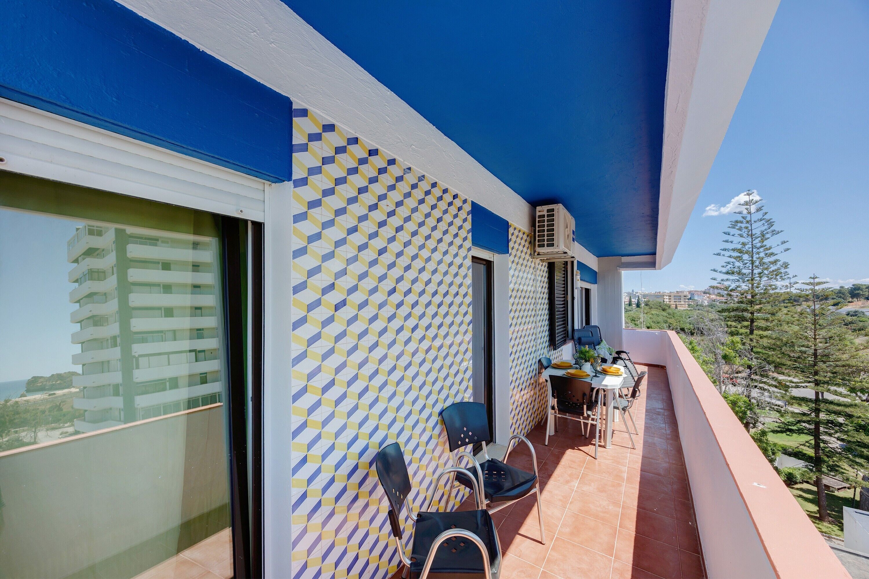 A balcony with a patterned wall, a dining table with chairs, and a view of a building and trees.