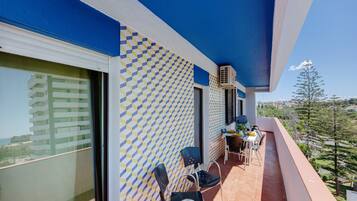 A balcony with a patterned wall, a dining table with chairs, and a view of a building and trees.