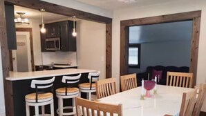 Un comedor con una mesa blanca, sillas de madera y una barra con taburetes.