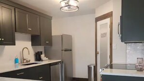 Una cocina con armarios oscuros, un refrigerador de acero inoxidable, un fregadero y una mesa de vidrio.