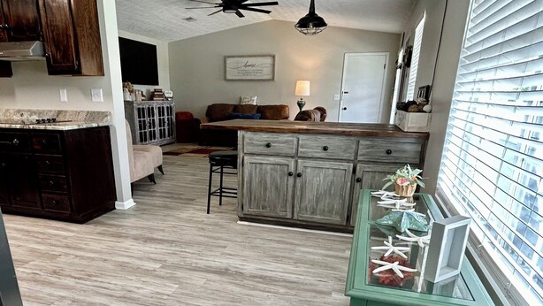A kitchen with wooden cabinets, a dining area with a sofa, and a view of a building through the window. - 3-bedroom house in tranquil Lynn Haven, beautiful sunsets, & minutes to PCB. (Lynn Haven)