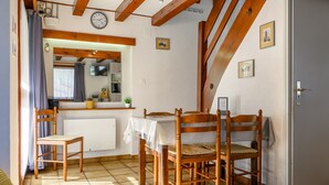 Une pièce chaleureuse avec une table à manger en bois, deux chaises en bois, un lit, un radiateur, une horloge et un coin cuisine avec une fenêtre.