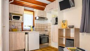 Une cuisine compacte équipée d’un micro-ondes, d’un four et d’un évier, une petite table avec une télécommande et des magazines, et un téléviseur fixé au mur.