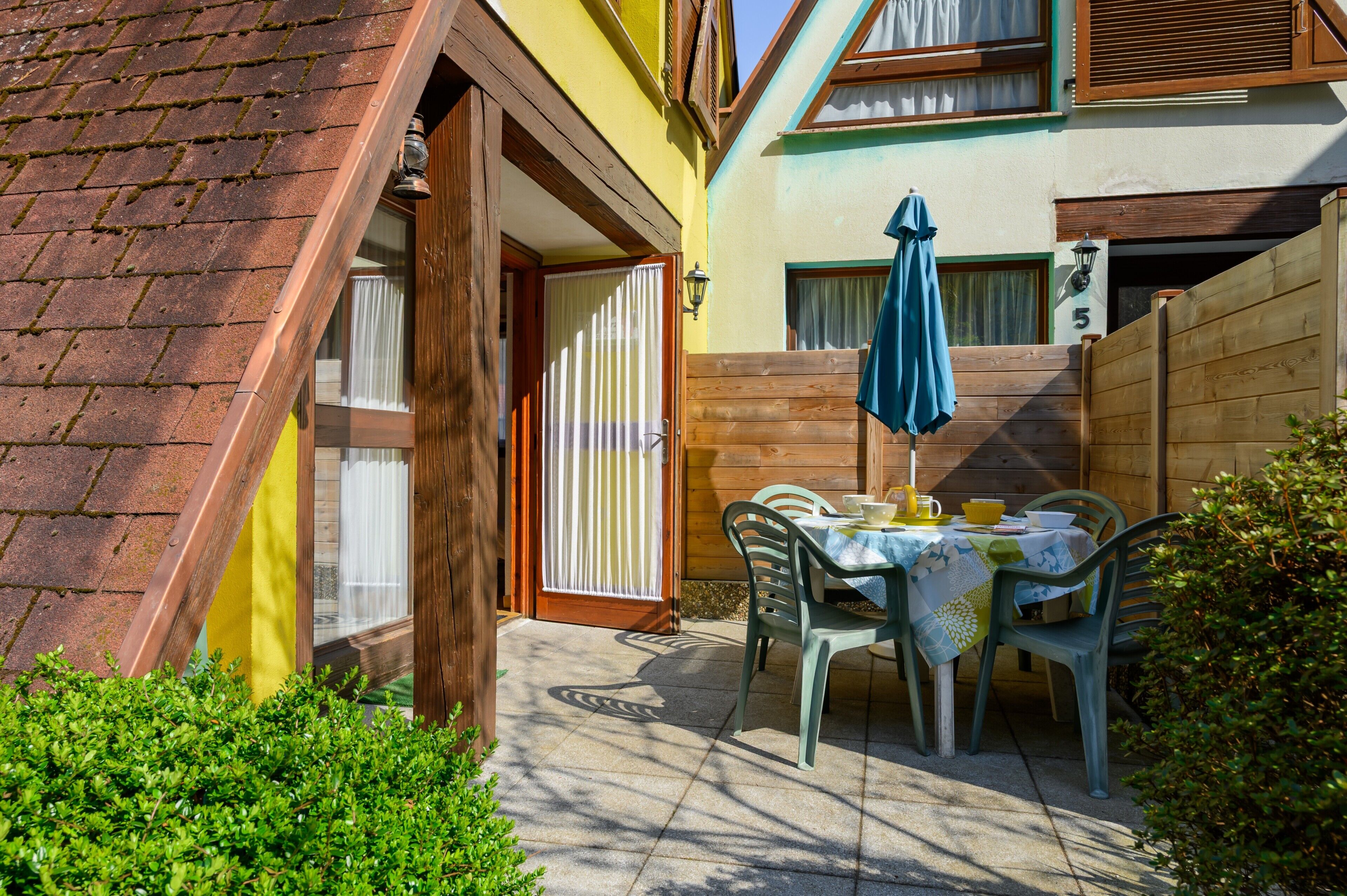 Un patio con una mesa y sillas, una cerca de madera y un edificio con un letrero con el número 5.