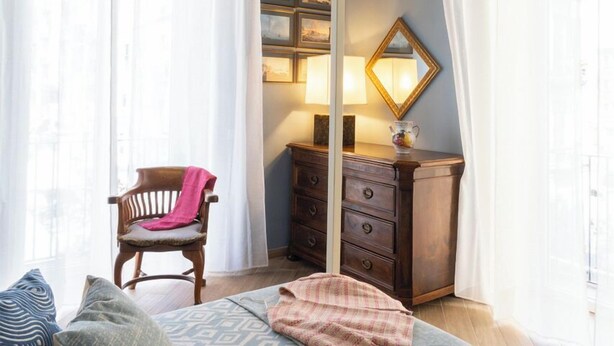 A bedroom with a wooden ceiling, a bed with patterned bedding, a chair, a dresser, and a mirror. - Maison Bayard - Two Bedroom Apartment, Sleeps 4 (Naples)