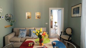 A living room with a sofa, a dining table with chairs, a vase with flowers, and two wall-mounted lamps. - Maison Bayard - Two Bedroom Apartment, Sleeps 4 (Naples)