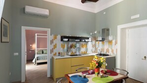 A compact kitchen with a dining area, a visible bed in the adjacent room, and a small island with a stove. - Maison Bayard - Two Bedroom Apartment, Sleeps 4 (Naples)