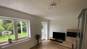 Ein modernes Wohnzimmer mit großen Fenstern, einem Flachbildfernseher, Holzböden und Einbauschränken.