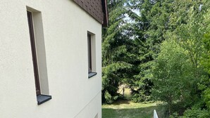 Ein schmaler Innenhof mit einem gepflasterten Weg, einem kleinen Gartenbereich mit Pflanzen und einem weißen Gebäude mit Fenstern und einer Tür.