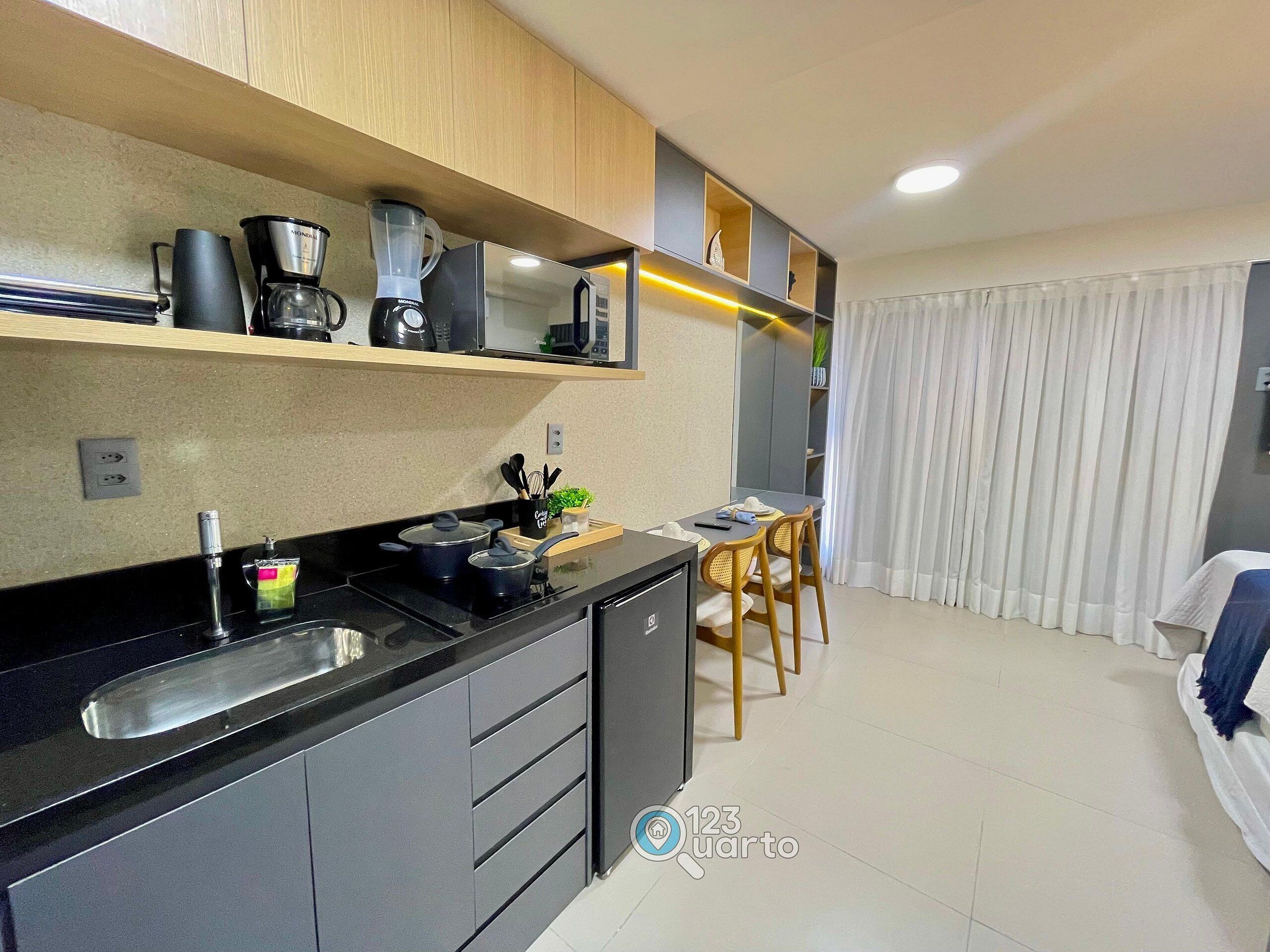 A modern kitchen with a black countertop, a coffee maker, a blender, and a sink. There is a dining area with a table and chairs.