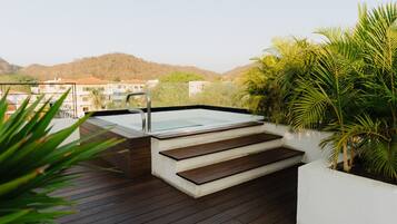 Une terrasse sur le toit avec un jacuzzi, des escaliers en bois et une végétation luxuriante tout autour.