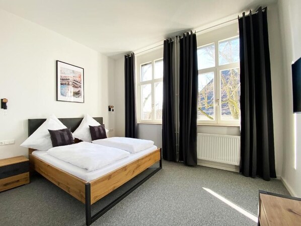 A hotel room with a bed, a window with curtains, a radiator, and a framed picture on the wall. - Best Boarding House (Hanau)
