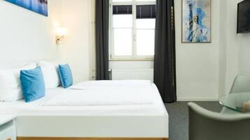 Habitación de hotel con cama, sillón, un cuadro de la Estatua de la Libertad y ventana con cortinas.