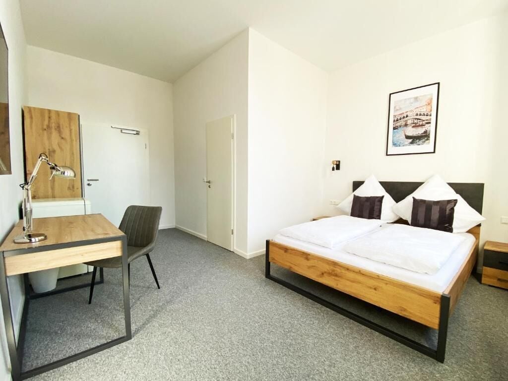 Ein Schlafzimmer mit einem hölzernen Bett, einem Schreibtisch, einem Stuhl und einem gerahmten Bild an der Wand.