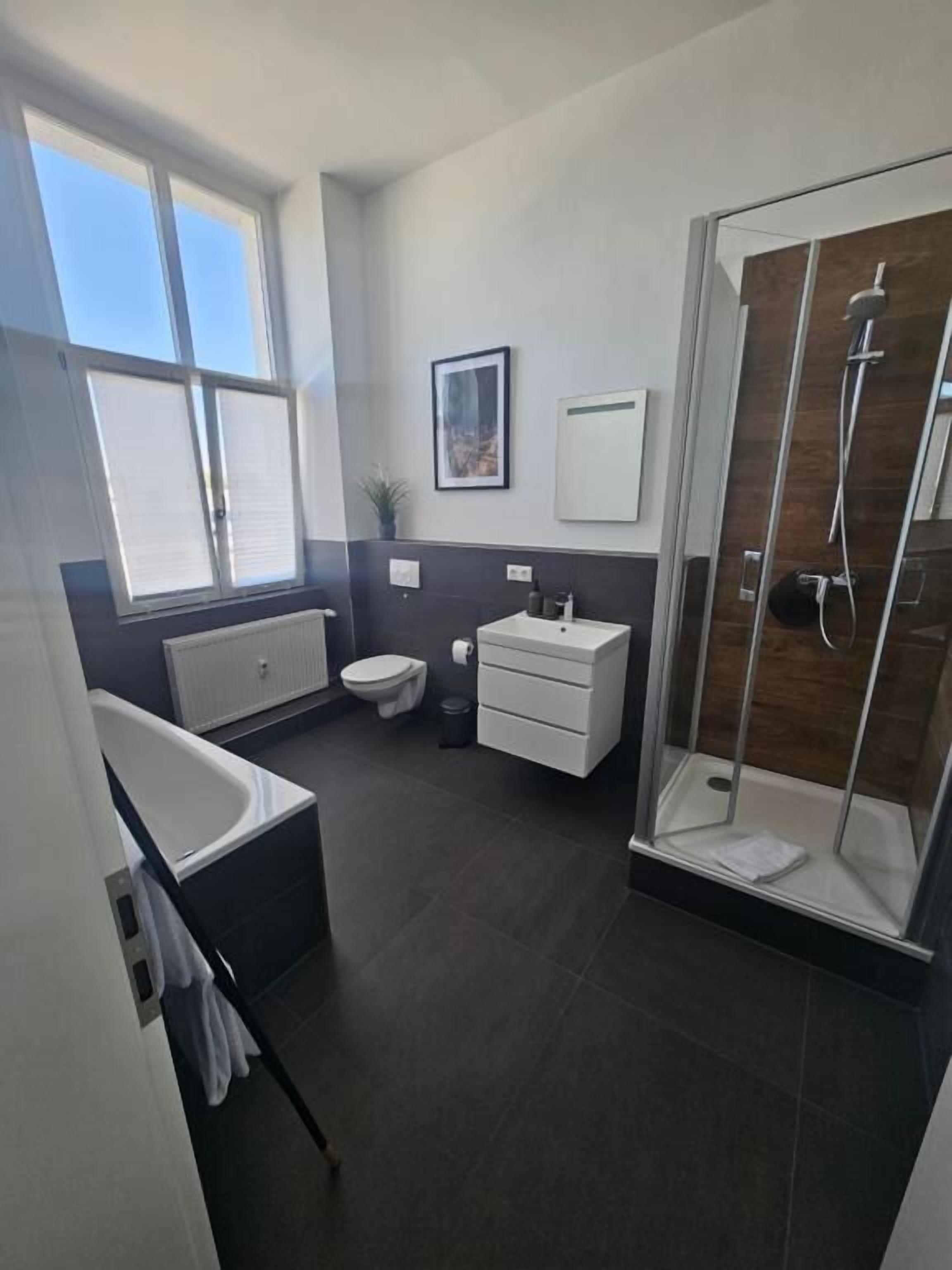 Un baño moderno con bañera, inodoro, tocador y ducha con mampara de vidrio.