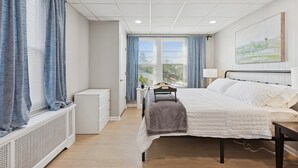 Un dormitorio con cama, mesita de noche, lámpara y ventana con cortinas.