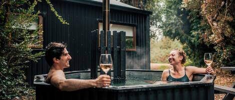 Dos personas en un jacuzzi con una estructura de madera al fondo.