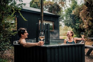 Two people in a hot tub with a wooden structure in the background.