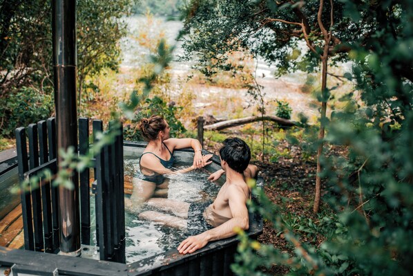 Two people in a hot tub outdoors surrounded by greenery.