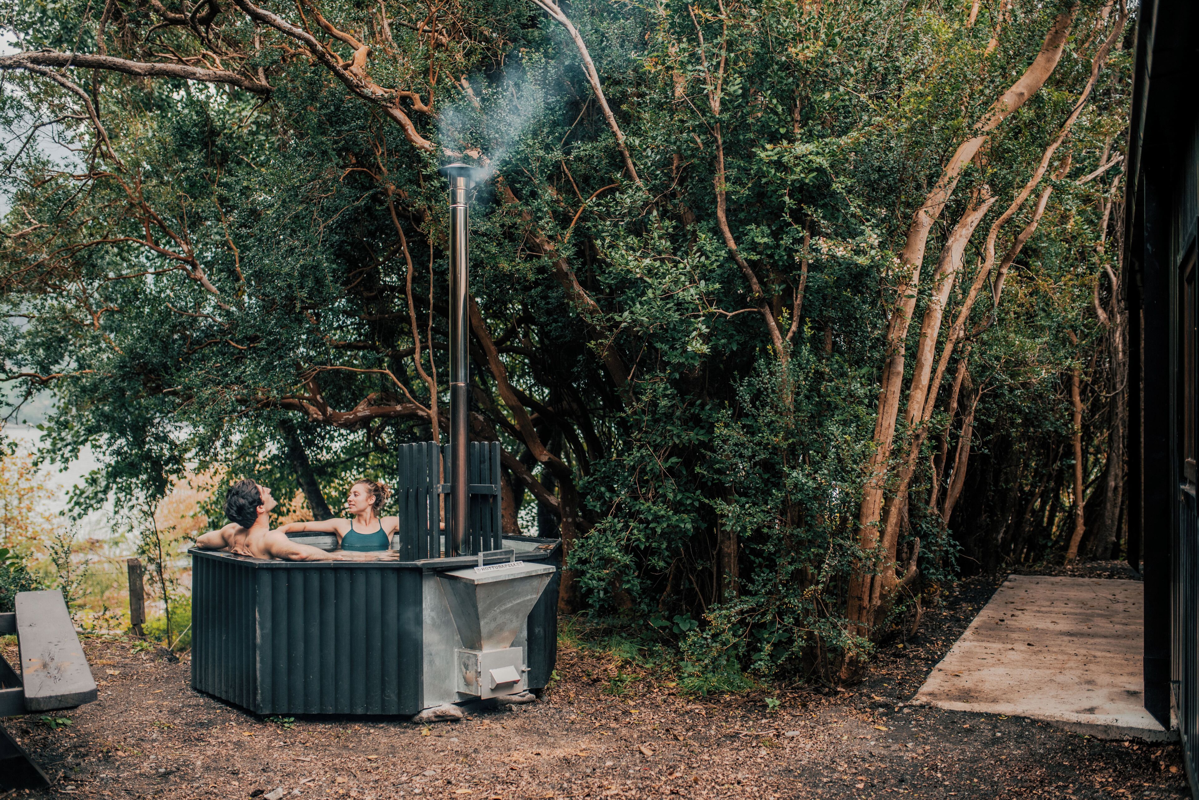 A hot tub in a wooded area with trees and a concrete path.