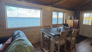 Uma cabana com uma mesa de jantar, cadeiras, um sofá e janelas amplas com vista para a água.