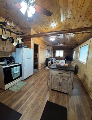 A cabin with a kitchen featuring a stove, refrigerator, and hanging pots.