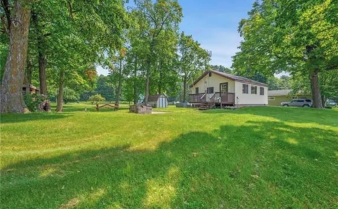 Einbungalow mit Veranda, umgeben von einem gepflegten Rasen und Bäumen.