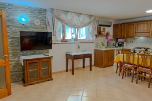 Eine Küche mit Fernseher, Holzschränken, einem Esstisch mit Stühlen und einem Fenster mit Vorhängen.