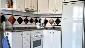 Eine Küche mit weißen Schränken, einem eingebauten Backofen, einem Kühlschrank und einer Spritzschutzwand mit diamantförmigem Muster.
