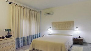 Une chambre à coucher comprenant un lit, des lampes de chevet, une table de chevet, une commode, une plante en pot et un élément décoratif mural.