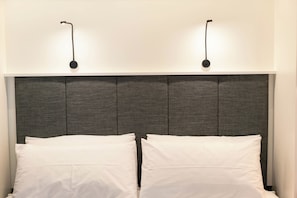 Ein Bett mit grauem Kopfteil, zwei weiße Kissen und zwei Wandleuchten.