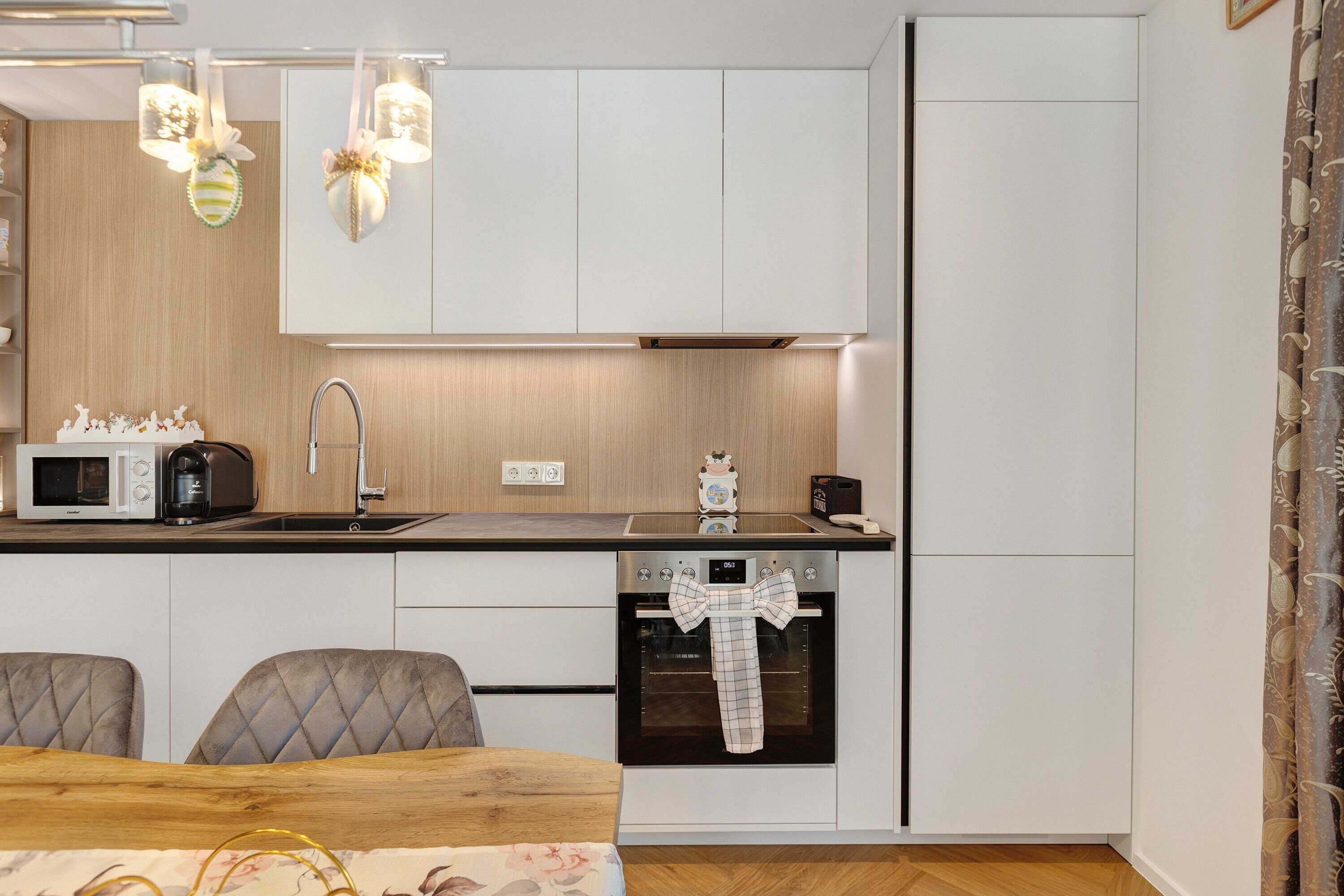 A modern kitchen with white cabinets, a microwave, a toaster, a sink, and an oven with a bow-tie towel.