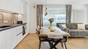 A modern kitchen with white cabinets, a wooden dining table, and a grey sofa in the living area. - Apartment 'Reichenau' with Private Terrace, Private Garden and Wi-Fi (Reichenau)