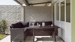 A covered patio area with a wicker sofa, a table, and a potted plant. - Apartment 'Reichenau' with Private Terrace, Private Garden and Wi-Fi (Reichenau)