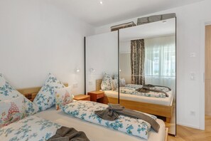 A bedroom with a large mirror, floral bedding, a wooden bed frame, a bedside table, and a nightstand. - Apartment 'Reichenau' with Private Terrace, Private Garden and Wi-Fi (Reichenau)