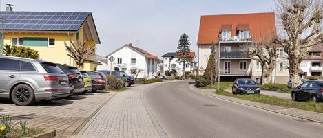 A residential street with parked cars, houses with solar panels, and a clear sky.
