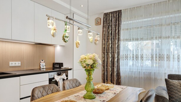A dining area with a wooden table, chairs, a vase with flowers, and a kitchen in the background. - Apartment 'Reichenau' with Private Terrace, Private Garden and Wi-Fi (Reichenau)