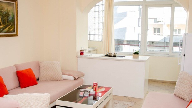 A modern living room with a sofa, a coffee table, and a view through a large window. - Cozy Apartment near Beach and City center Durres Vollga (Durres)