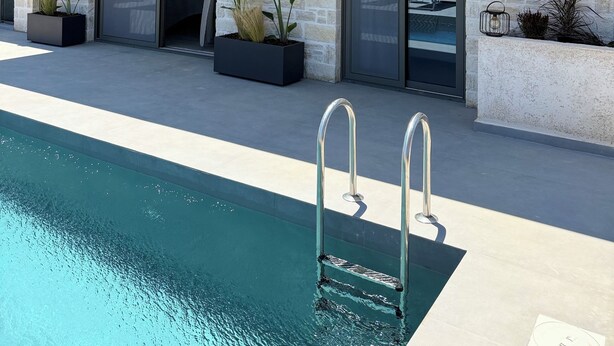 Una casa moderna de dos pisos con piscina, ventanas amplias y mobiliario exterior.