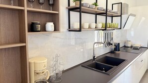 Una cocina moderna con estantes de madera, una cafetera y un lavamanos negro.