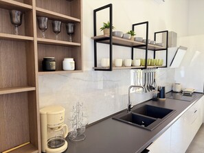A modern kitchen with wooden shelves, a coffee maker, and a black sink. - Sunrise Village Aptera Private Pool Villa No1 - Horizon (F477+79, Souda)